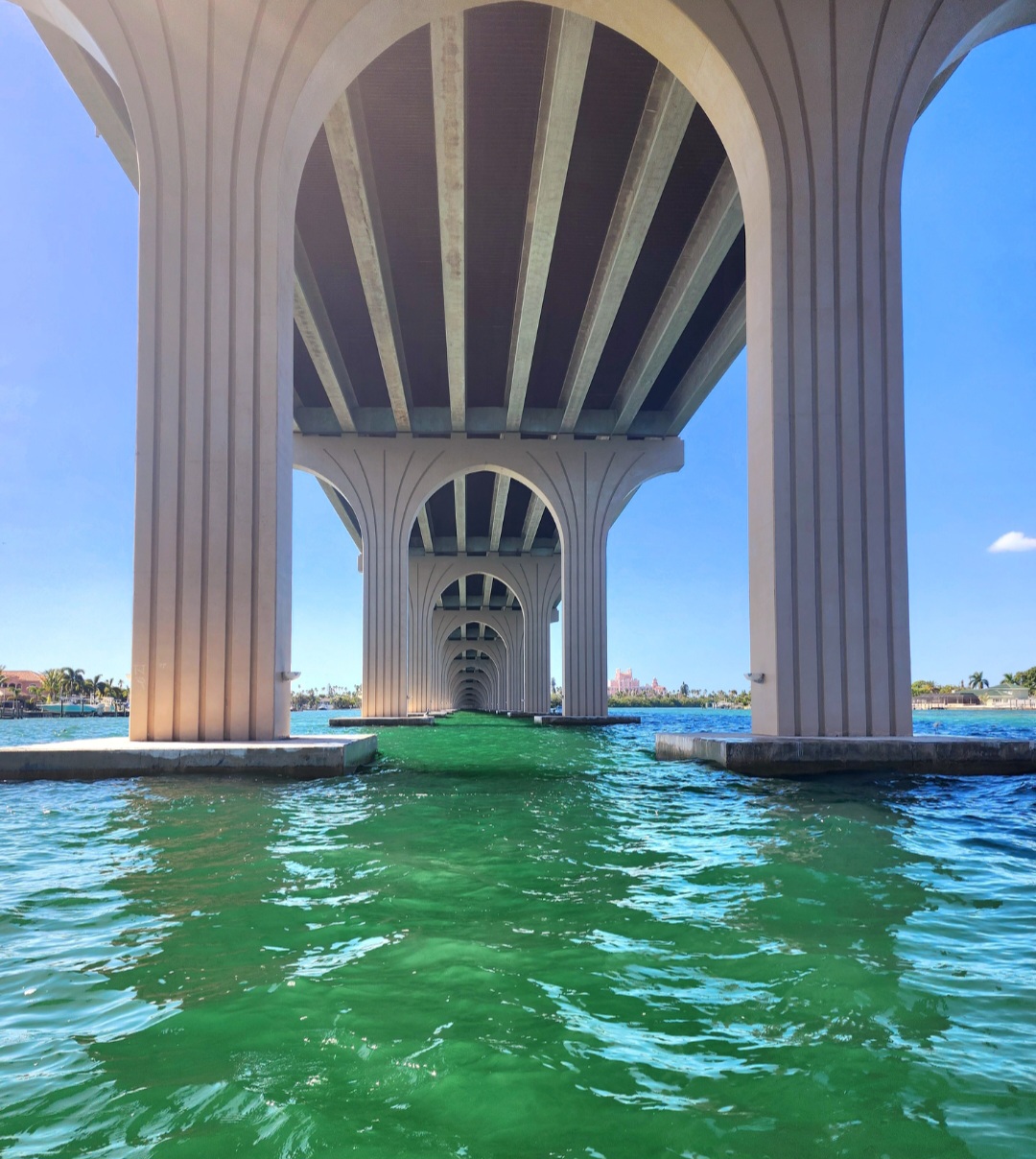 Looking beneath the Pinellas Bayway bridge where the columns and arches repeat into a long corridor over green water near St. Pete Beach, Florida