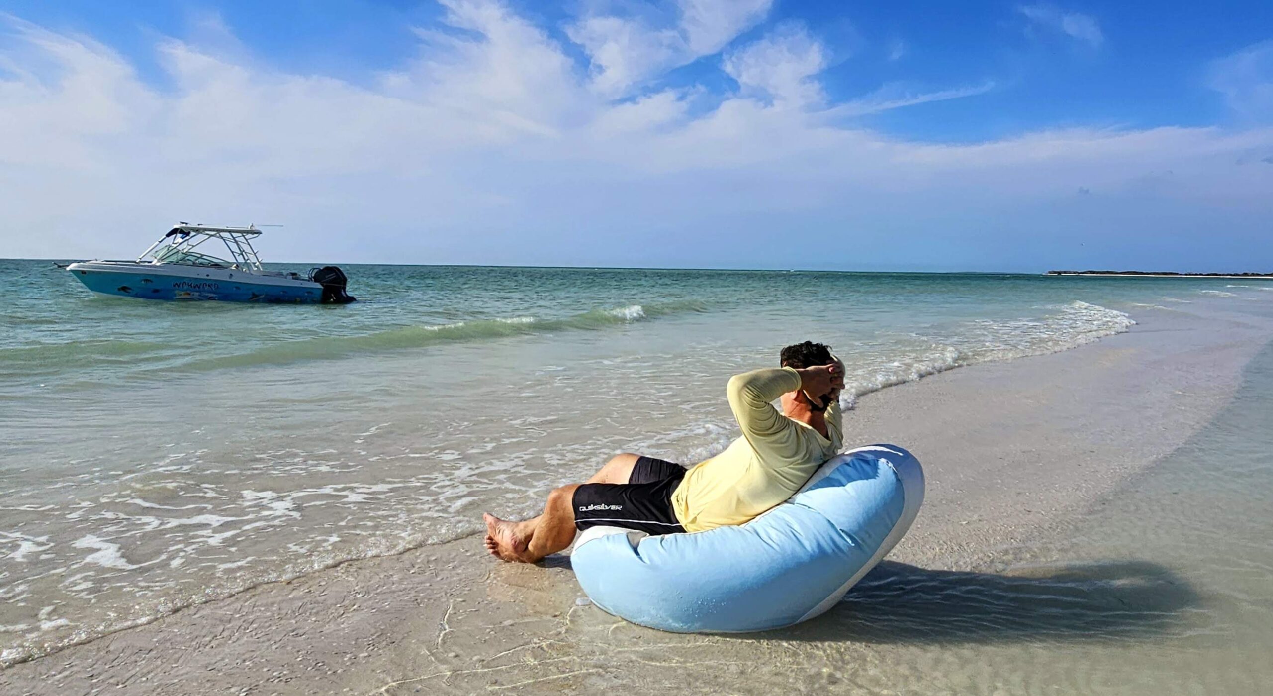 A guest relaxing in a bean bag chair at the water&rsquo;s edge with the charter boat anchored behind, near Clearwater, Florida